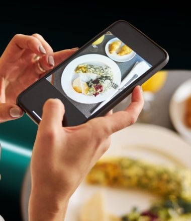 Hands holding phone taking photo of food